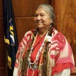 Patsy Whitefoot stands in state capital chambers beside a flag